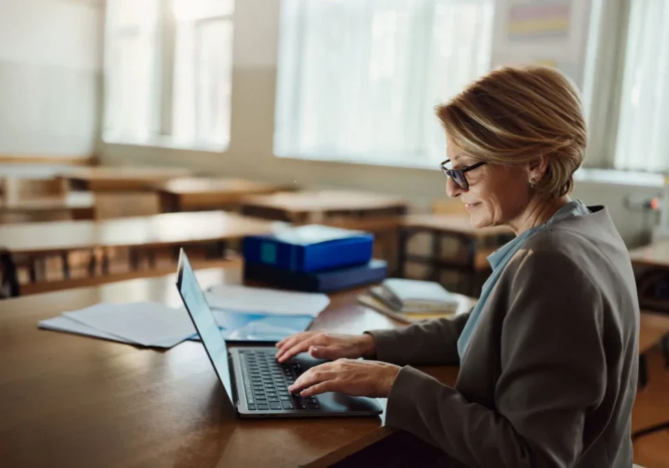 Teacher working on laptop in empty classroom
