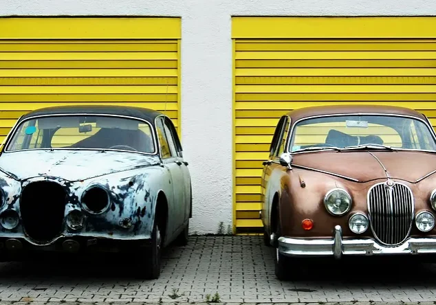Two vintage cars parked by yellow garage doors
