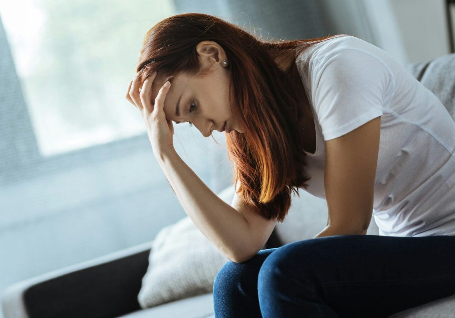 Stressed woman sitting on couch, head in hand